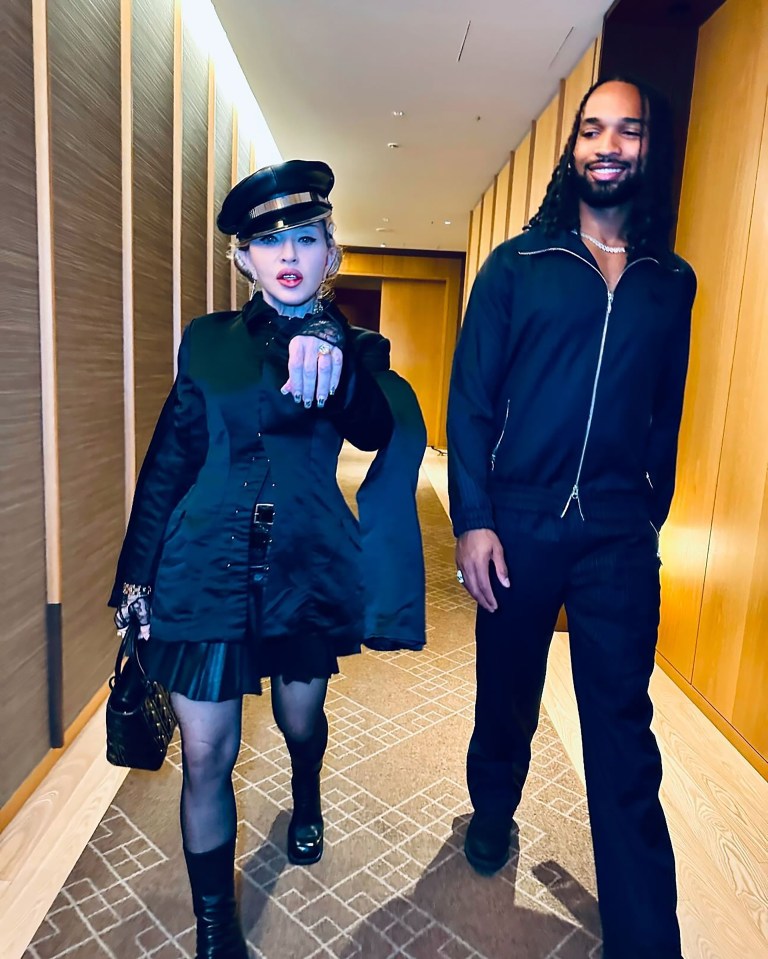 Madonna and her partner walking down a hallway; she is wearing a large diamond ring.