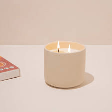 A lit double-wick candle in a beige ceramic jar.