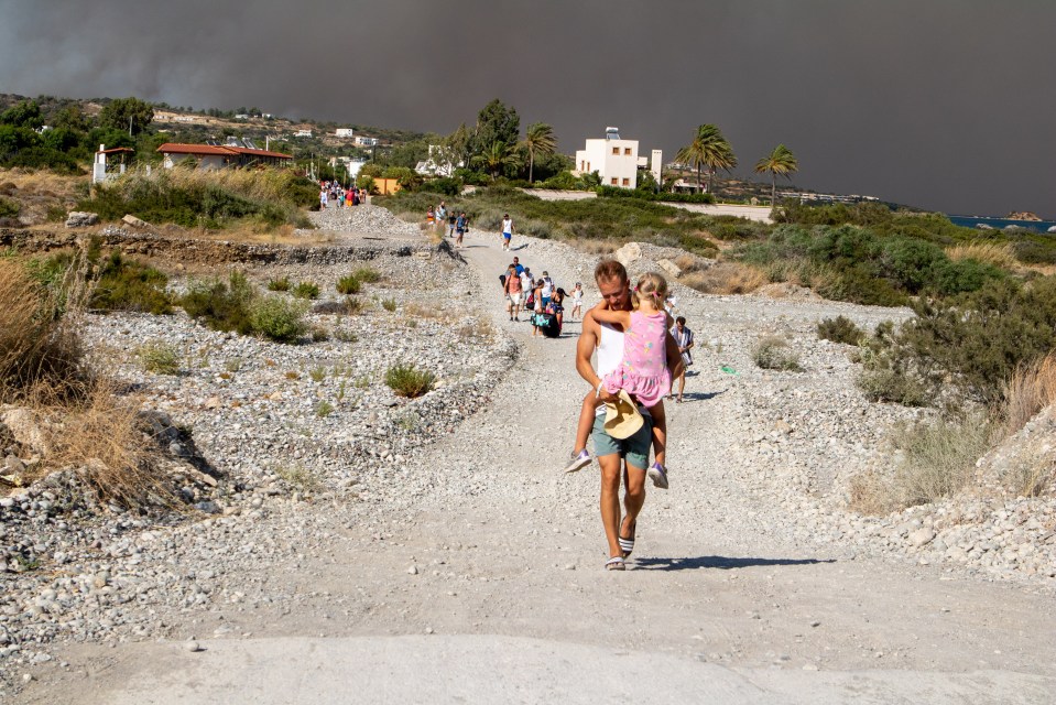 A man carried a child after fleeing from his hotel in Rhodes