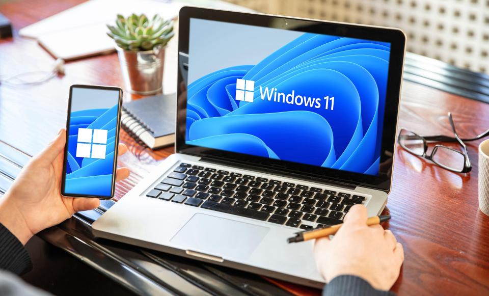 a person holding a cell phone in front of a laptop that says windows 11