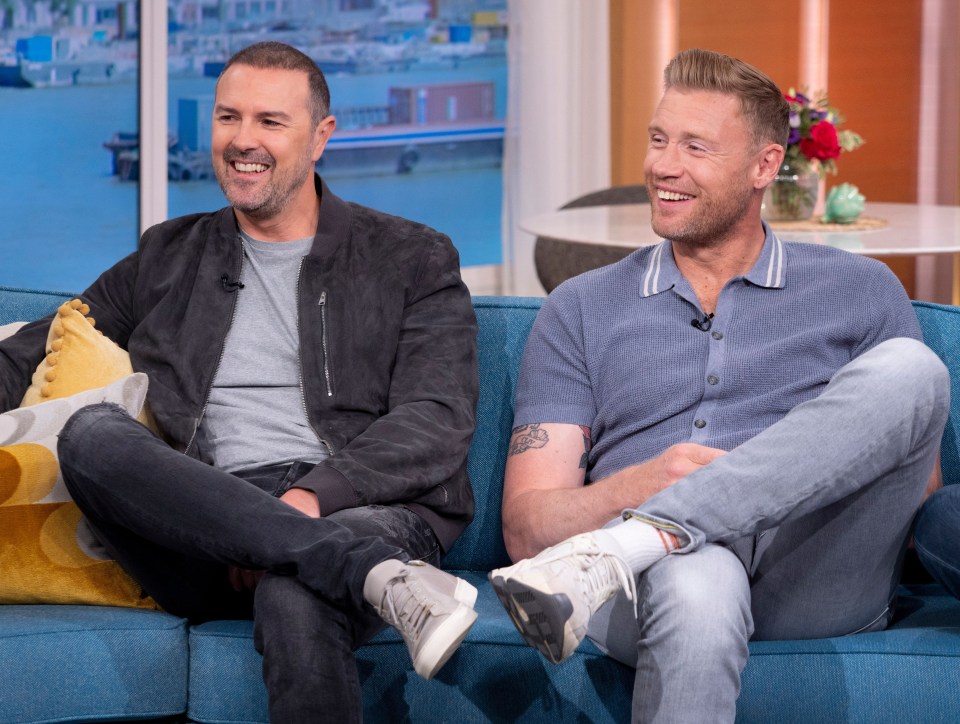 two men are sitting on a blue couch and smiling