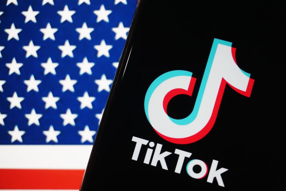 TikTok logo on a phone screen with a blurred US flag in the background.