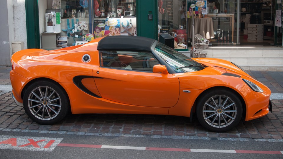 Orange Lotus Elise parked on a cobblestone street.