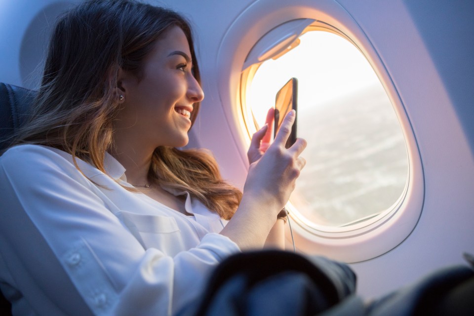 a woman looks out of an airplane window while using her phone