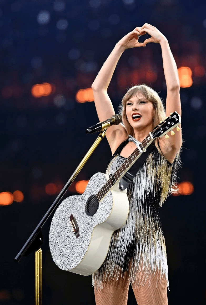 a woman is holding a guitar and making a heart shape with her hands