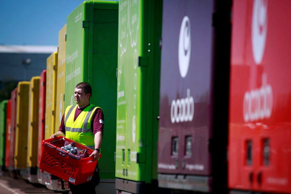 a man in a yellow vest carrying a red basket stands in front of a row of cargo trucks that say coodo