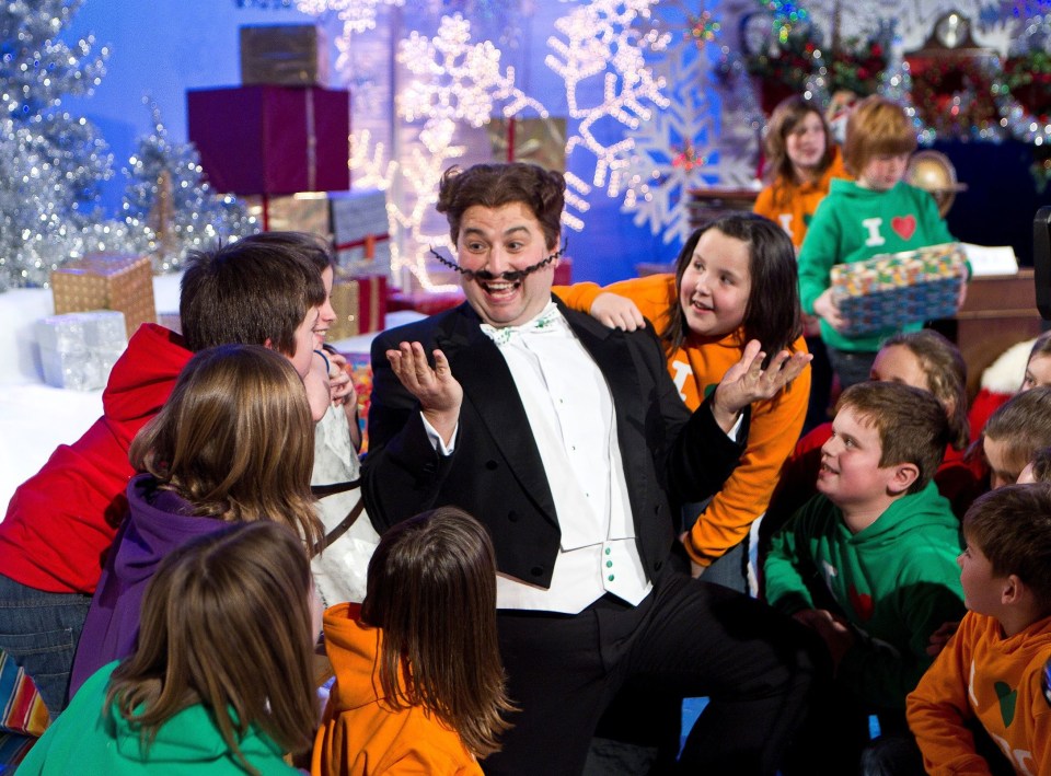 a man in a tuxedo with a fake mustache is surrounded by children