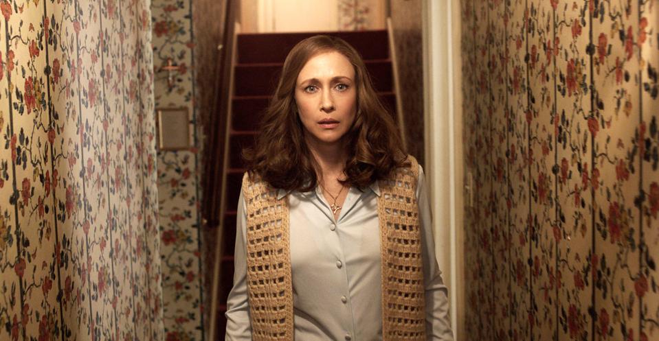 a woman standing in a hallway with floral wallpaper