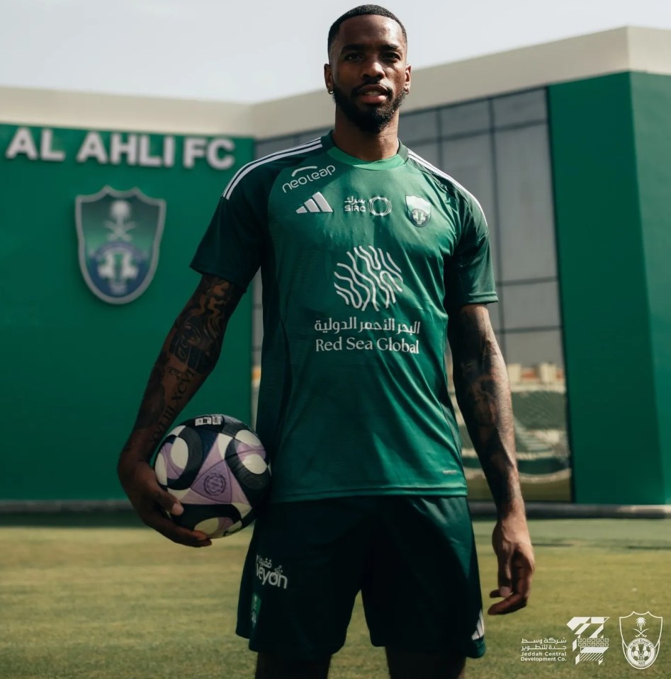 a man holding a soccer ball in front of a building that says al ahli fc