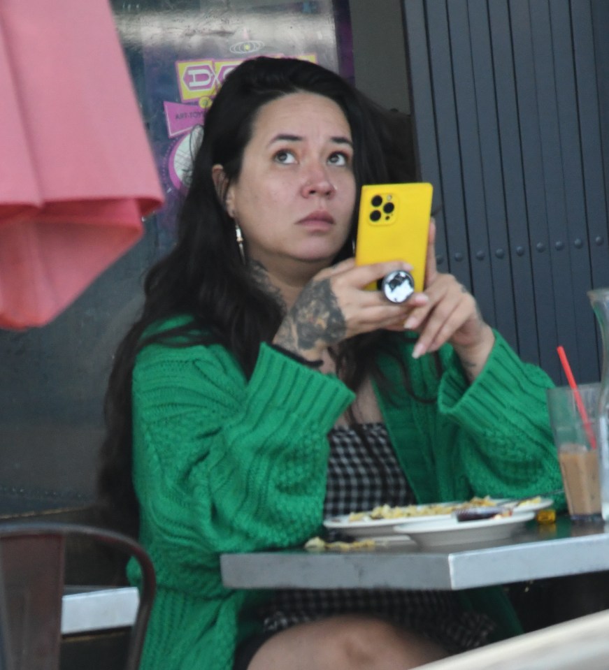 a woman in a green sweater sits at a table looking at her phone