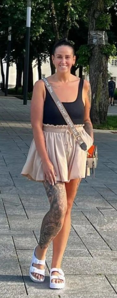a woman wearing a black tank top and a beige skirt stands on a sidewalk