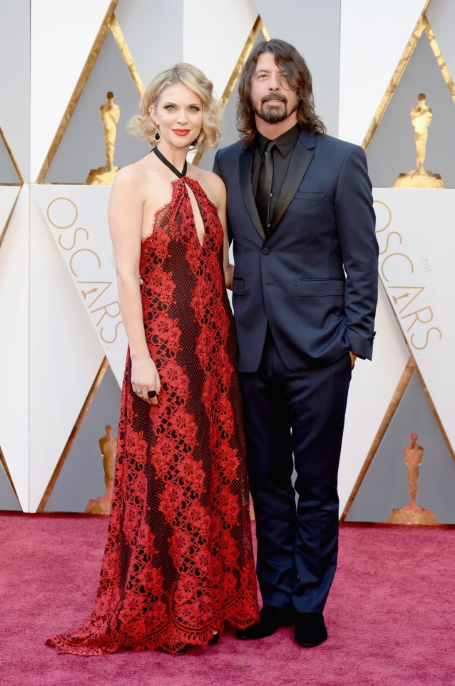 a woman in a red dress stands next to a man in a suit on a red carpet that says oscars