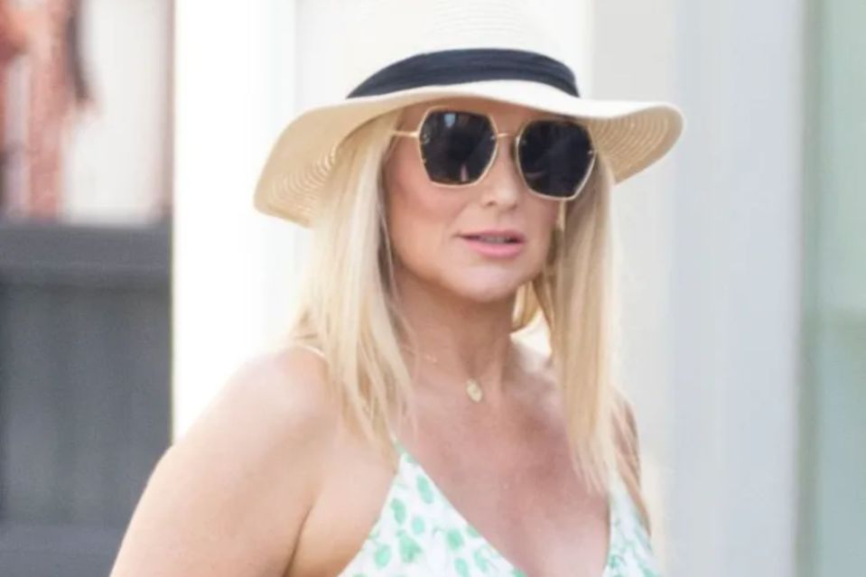 a woman wearing a hat and sunglasses is walking down the street .