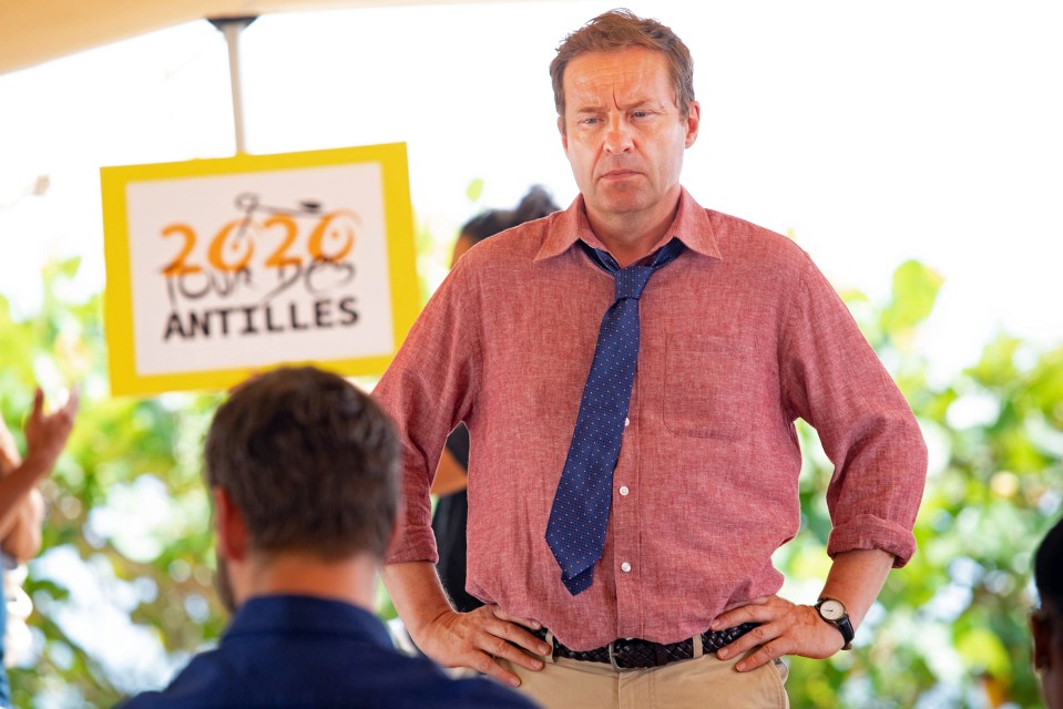 a man stands in front of a sign that says 2020 tour des antilles