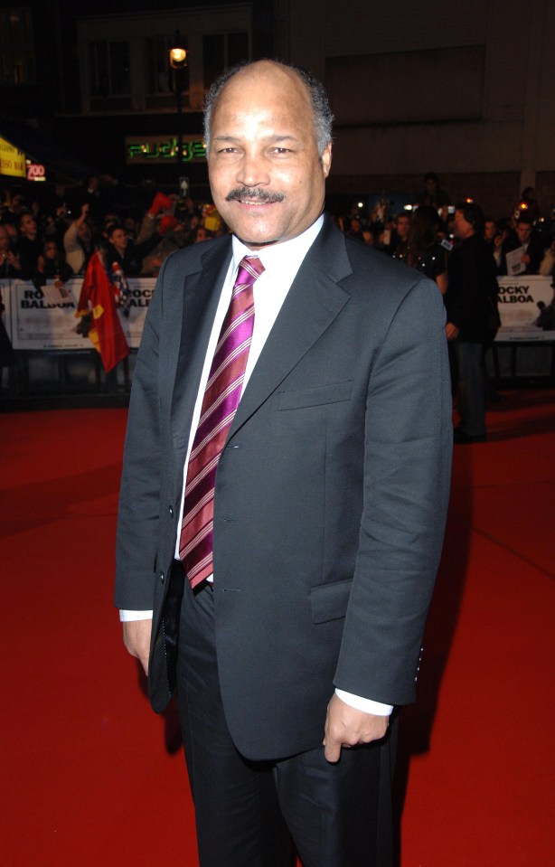 a man in a suit and tie stands on a red carpet in front of a sign that says rocky balboa