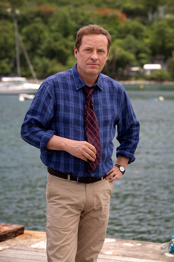 a man in a blue plaid shirt and tie stands in front of a body of water