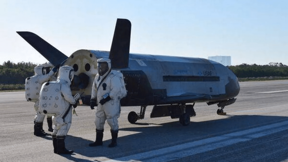 a group of people in protective suits are standing next to a drone on a runway .