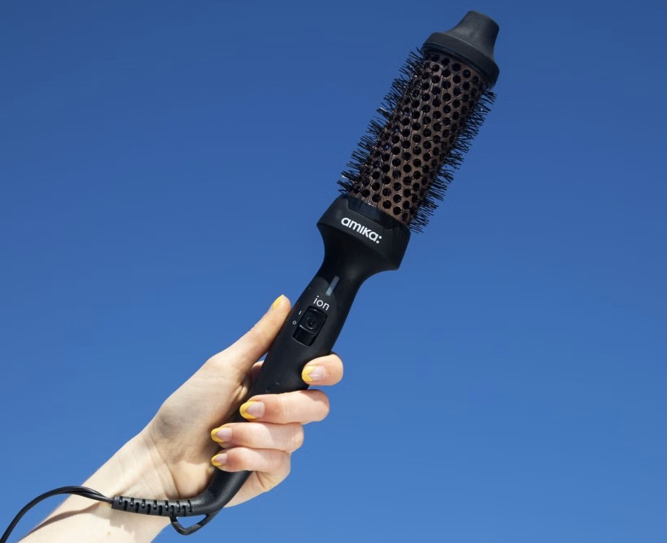 Hand holding Amika ion round hair brush against a blue sky.