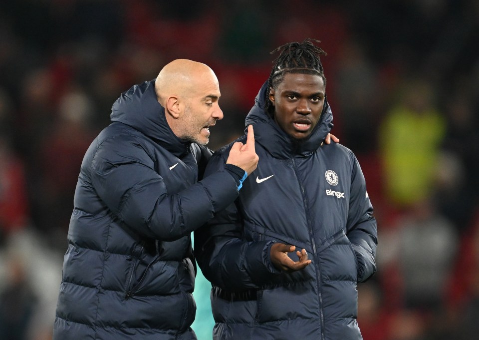 a man wearing a jacket with the chelsea logo on it talks to another man