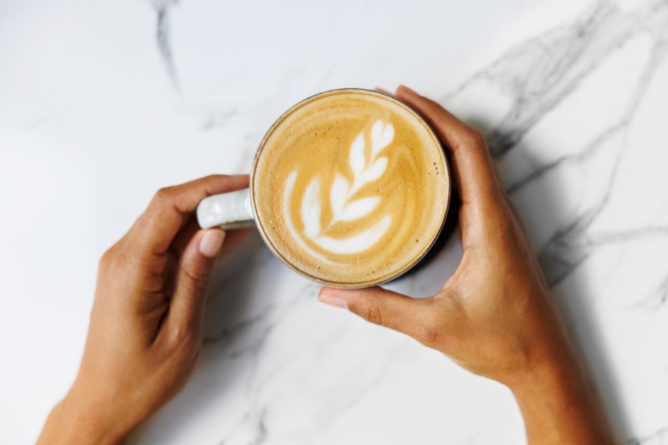 a person is holding a cup of coffee with a leaf design on it