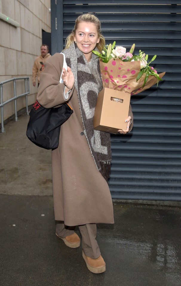 a woman in a brown coat is holding a box of flowers