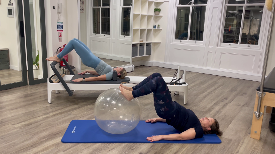 Two women performing Pilates exercises; one on a reformer, one using a stability ball.