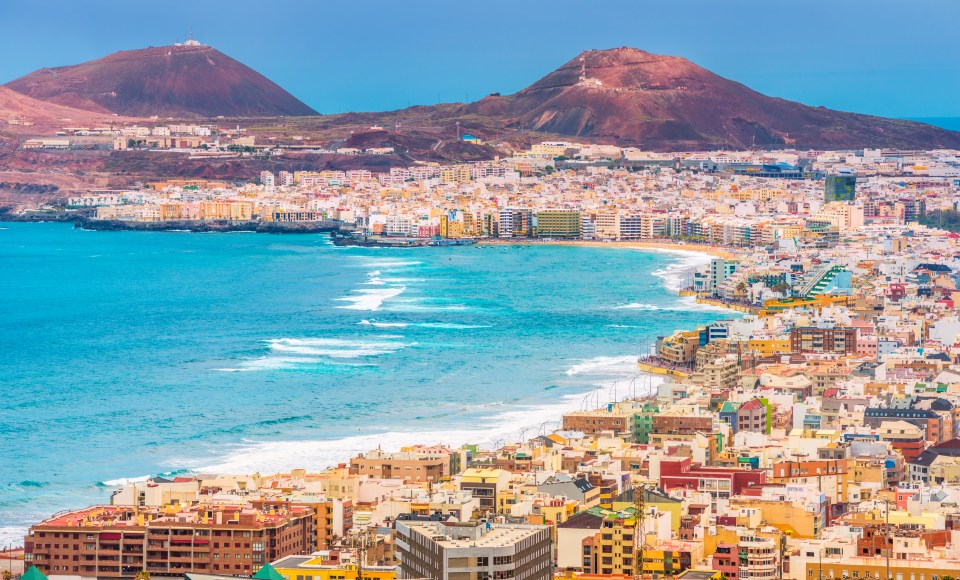 Aerial view of Las Palmas de Gran Canaria, showing the city, beach, and mountains.
