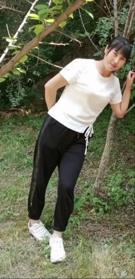 Woman in white shirt and black pants standing in a wooded area.