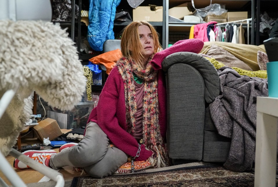 Bianca Jackson, chained and sitting on the floor in a cluttered room.