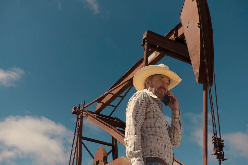 Billy Bob Thornton as Tommy Norris from the series "Landman," on a cell phone, near an oil derrick.