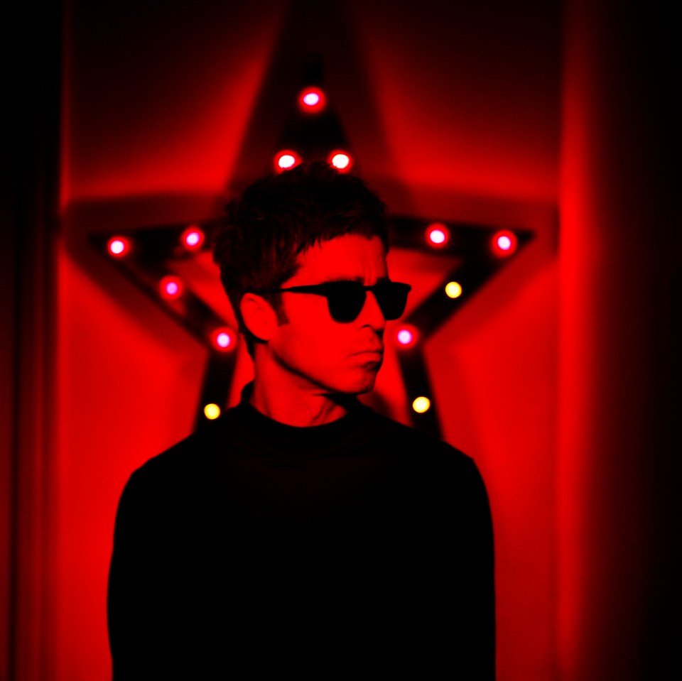 Liam Gallagher in red light, in front of a red star.