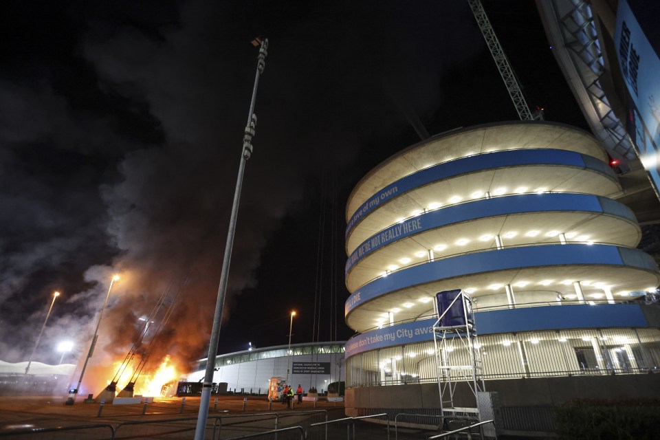 Firefighters extinguishing a fire at a merchandise kiosk outside a stadium.