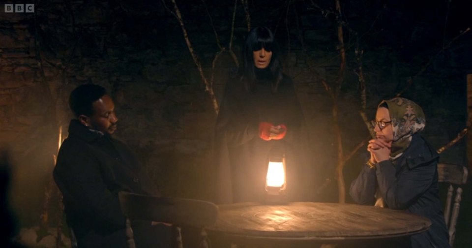 Three contestants on The Traitors sit around a table at night, illuminated by a lantern.