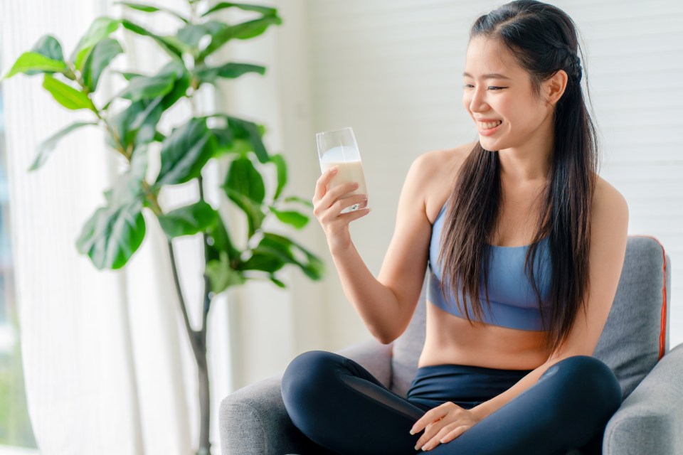 Woman in sportswear smiling while drinking a protein shake.