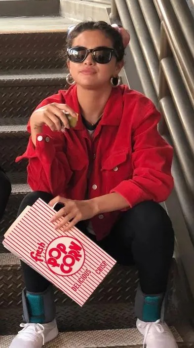Selena Gomez and a man sitting on steps, eating popcorn.