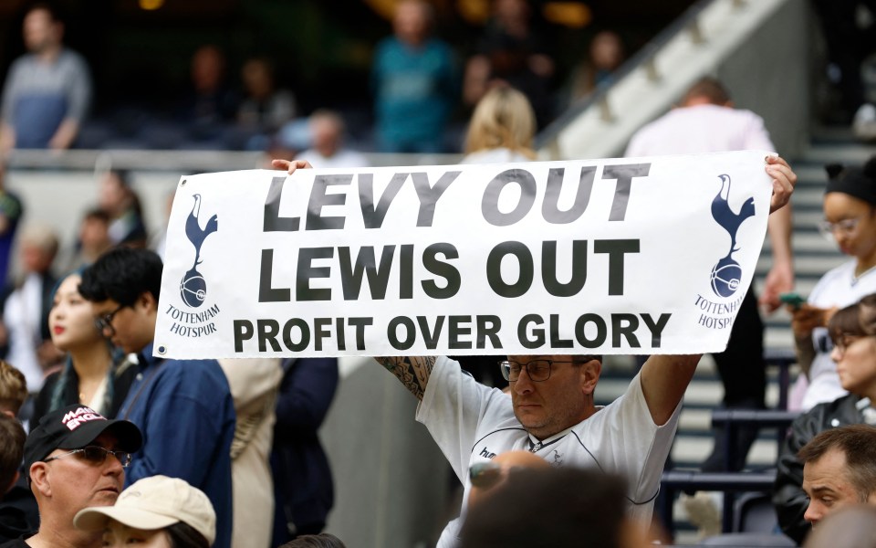 A Tottenham Hotspur fan holds a sign that reads "Levy Out Lewis Out Profit Over Glory".