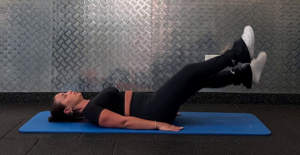 Woman wearing ankle weights doing leg raises on a mat.