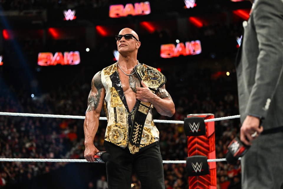 Dwayne "The Rock" Johnson in a wrestling ring holding a championship belt.