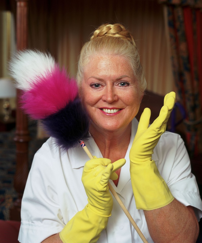 Kim Woodburn holding a duster and wearing yellow gloves.