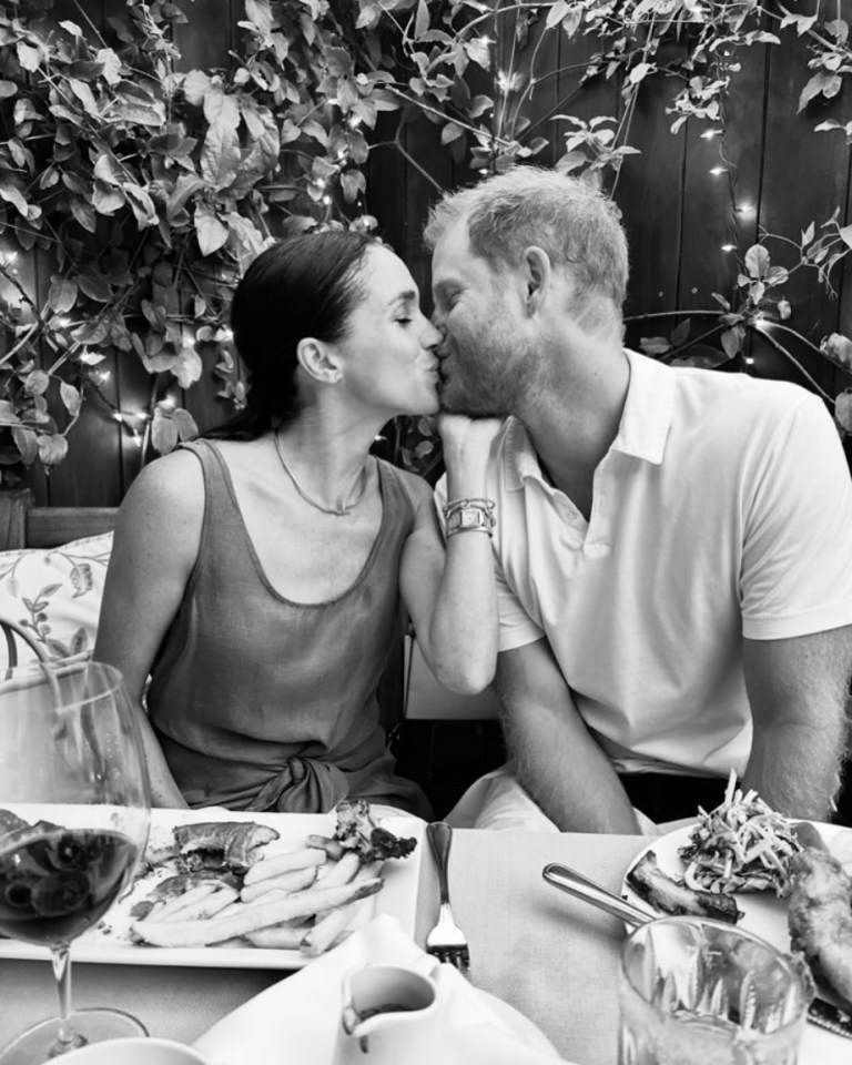 Black and white photo of Meghan Markle and Prince Harry kissing at a table with food.