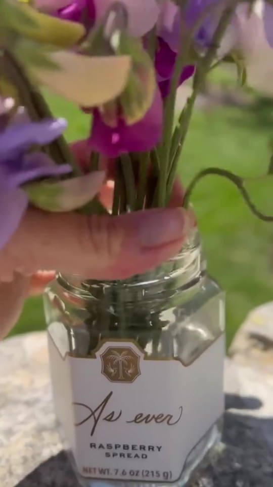 A hand placing sweet peas in an As Ever raspberry spread jar.