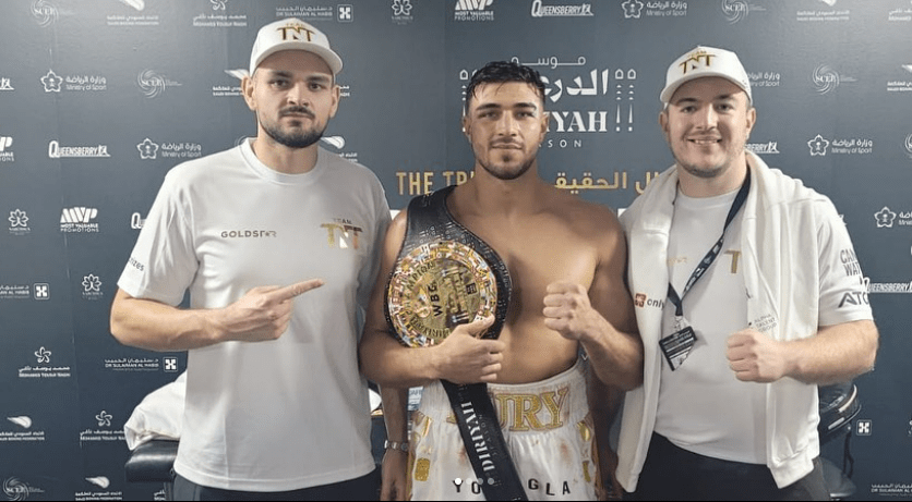Boxer with championship belt flanked by two men.