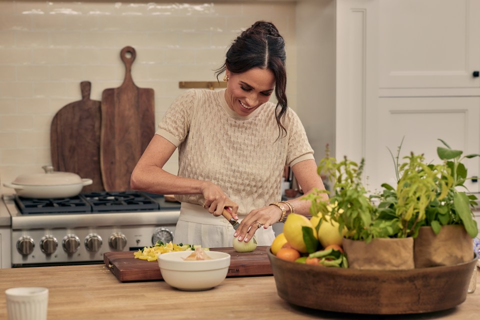 Meghan Markle chopping an onion in a kitchen.