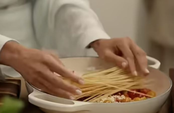 Hands adding spaghetti to a pan of sauce.