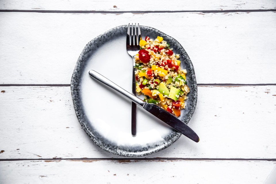 A plate of bulgur salad with avocado and bell peppers, arranged to look like a clock showing a specific time.  A fork and knife are placed on the plate as clock hands.