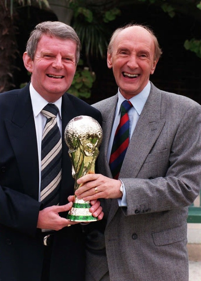 Two sportscasters holding a replica World Cup trophy.