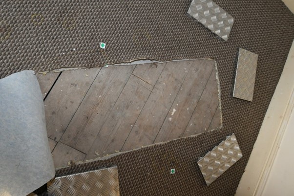 Cut carpet revealing wood floorboards.