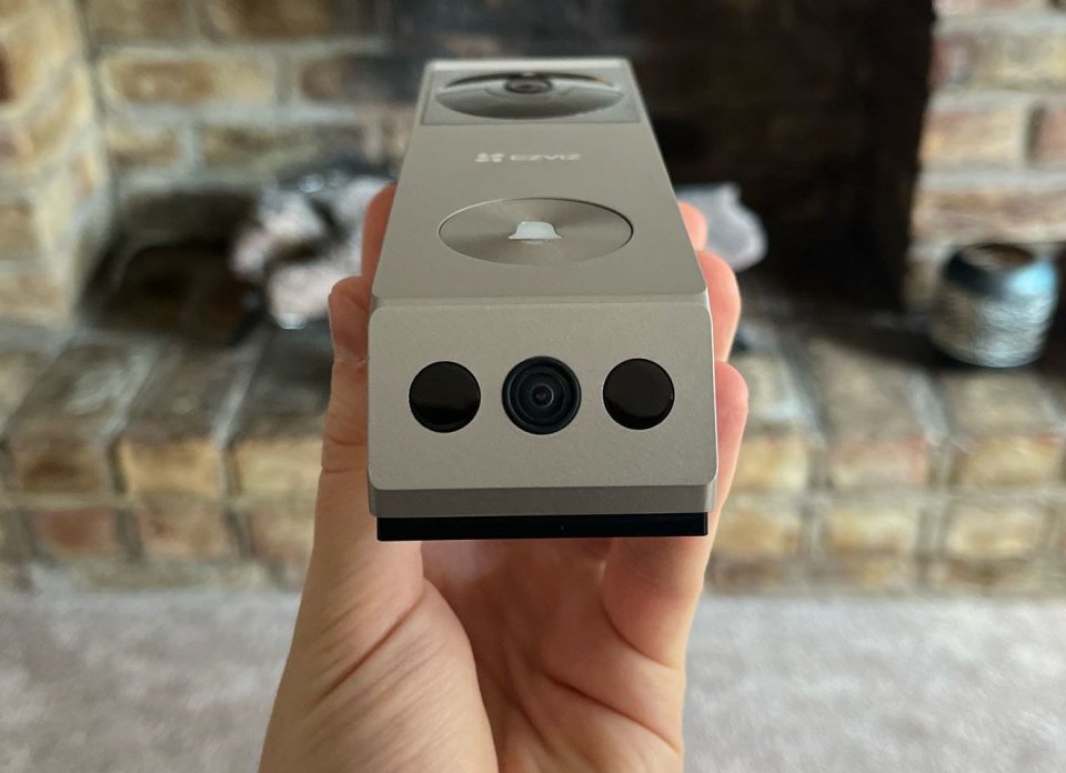 Hand holding a beige Ezviz doorbell camera.