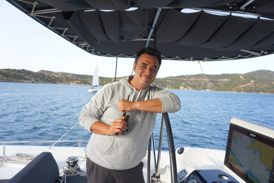 Man smiling at the helm of a yacht in Greece.