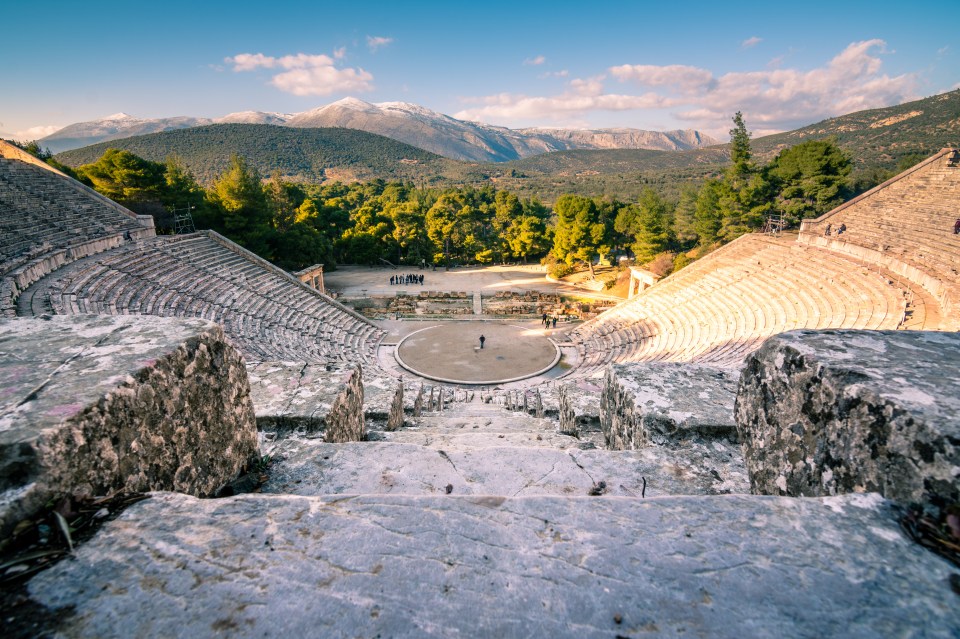 Ancient Greek amphitheater with mountains in the background.